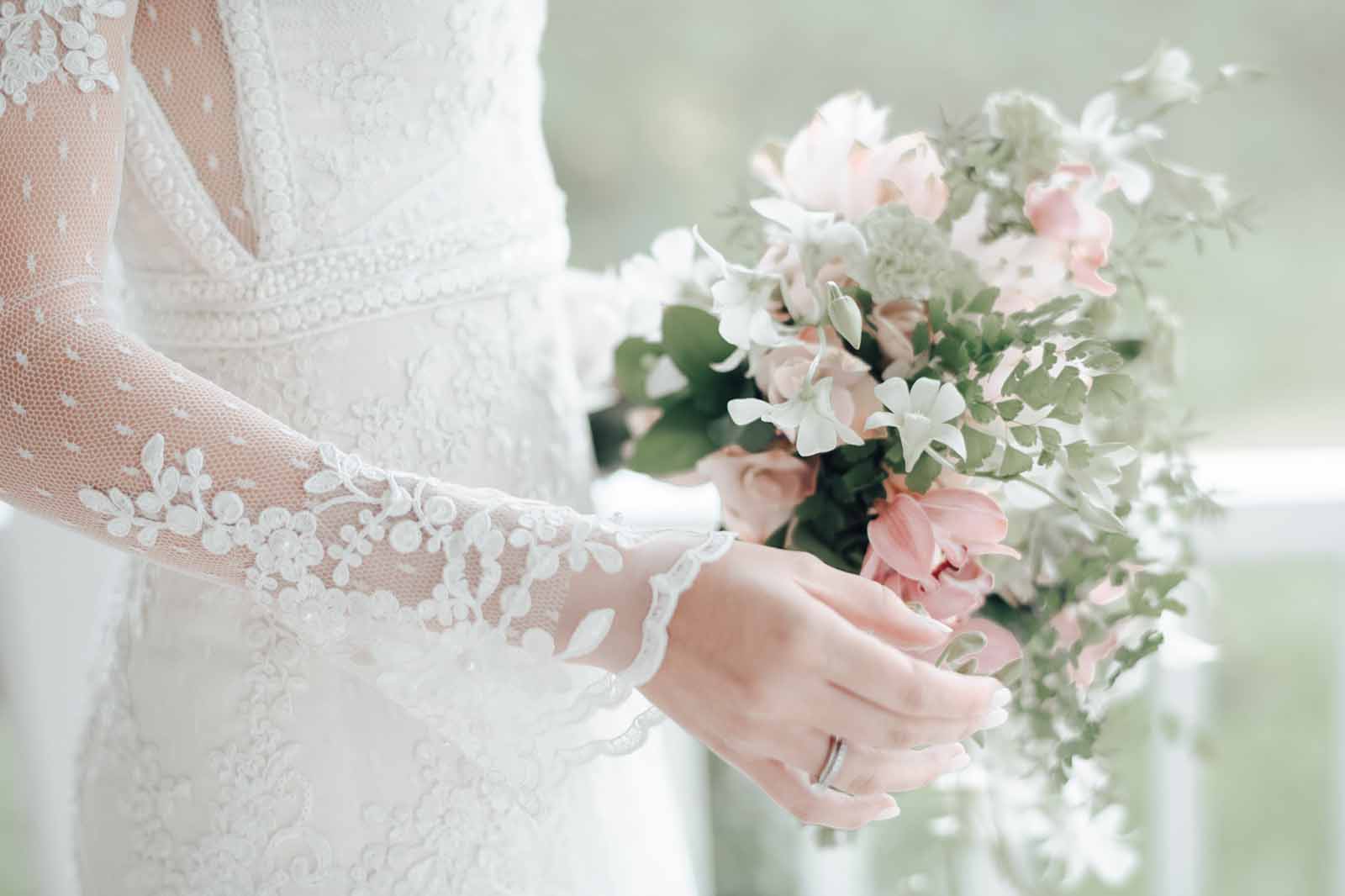 Destaque das mãoes de uma noiva segurando buquet de flores.